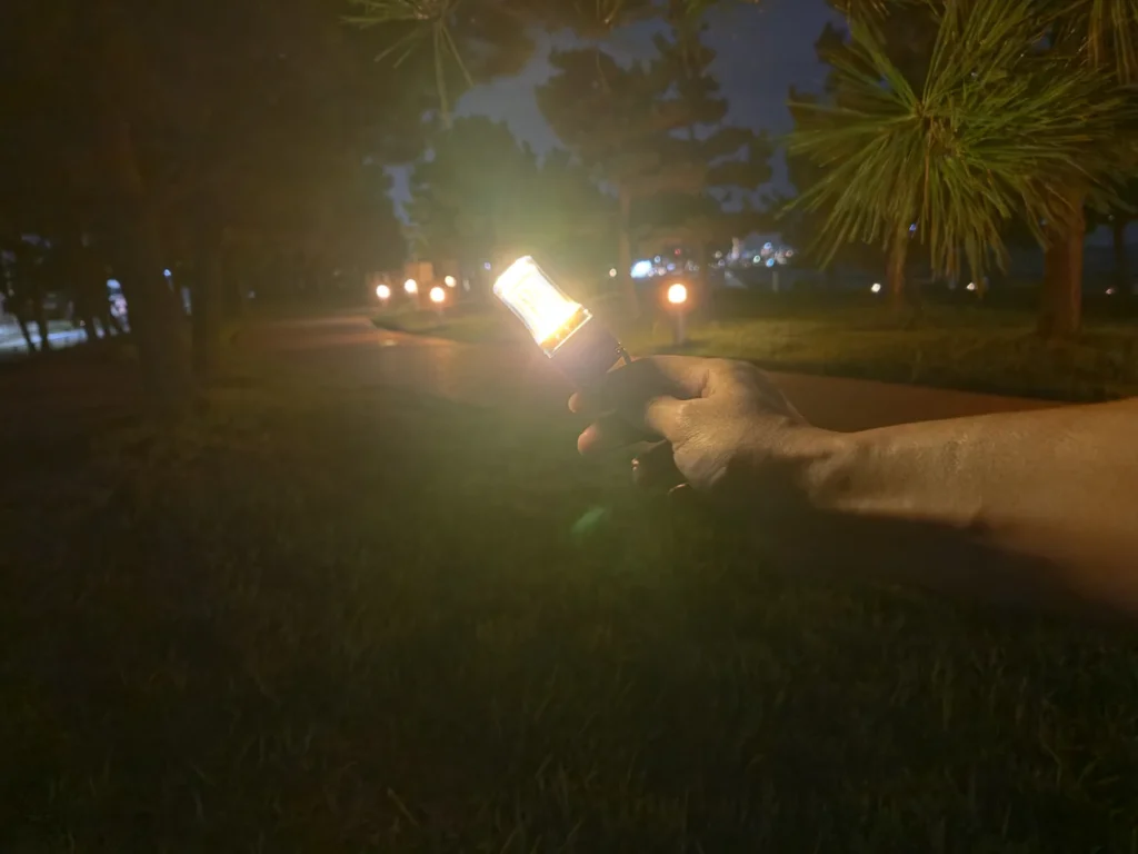 夜の公園の遊歩道で、点灯したFLEXTAIL ZERO LANTERNを腕を伸ばして持つ