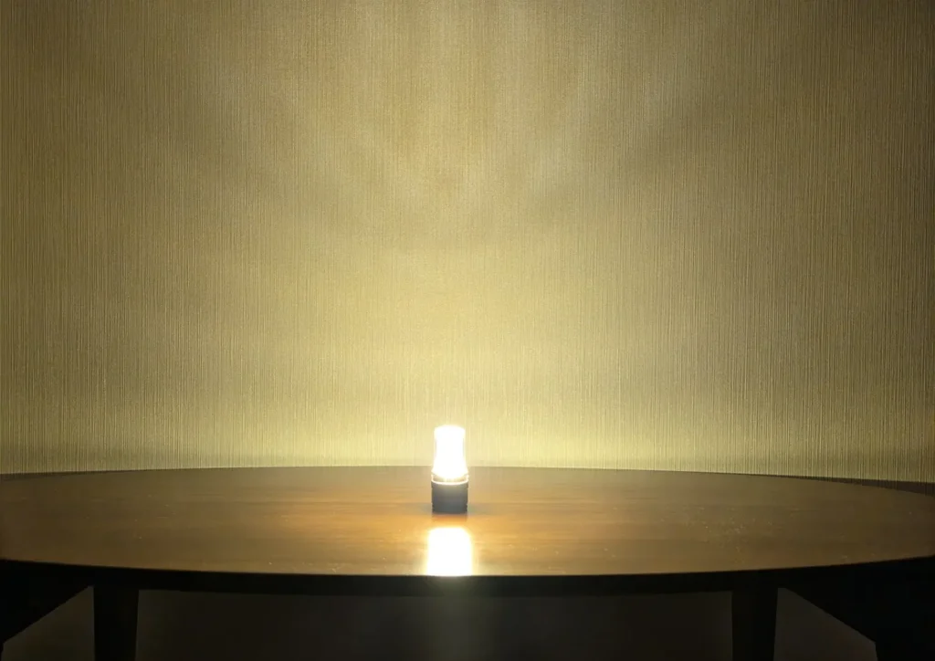 テーブルに置いたFLEXTAIL ZERO LANTERNのランタンモード最大。電球色の光が壁一面に広がる