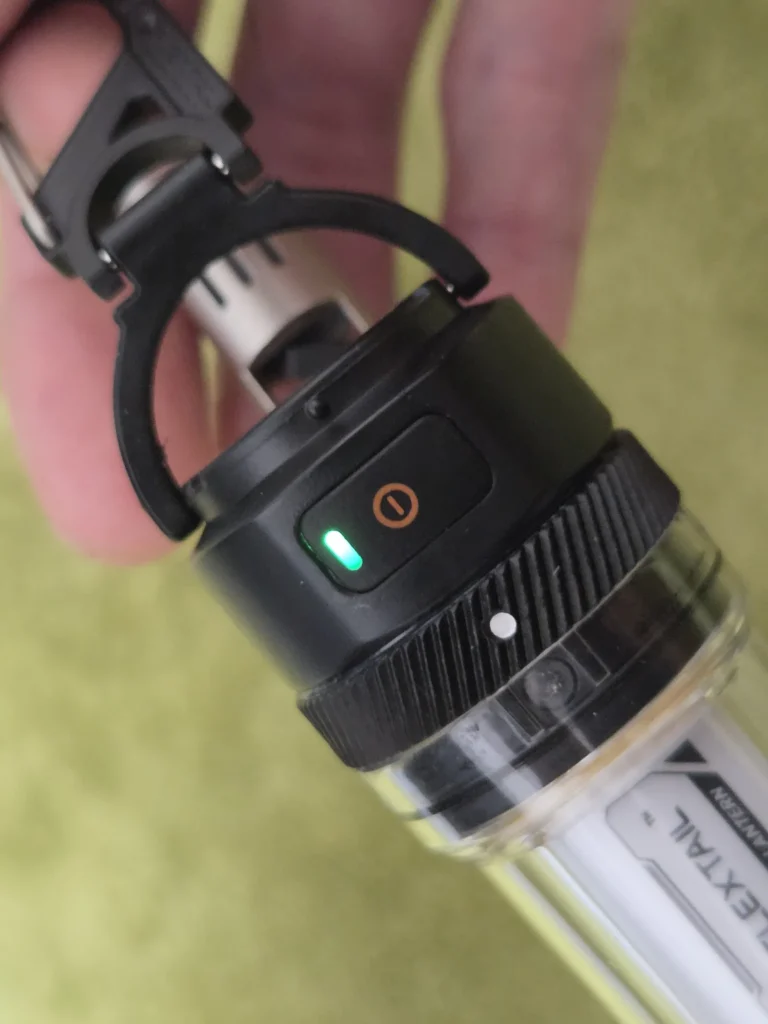 満充電になり、電源ボタンにある小窓が緑に光っている本体。奥にUSBケーブルのプラグ